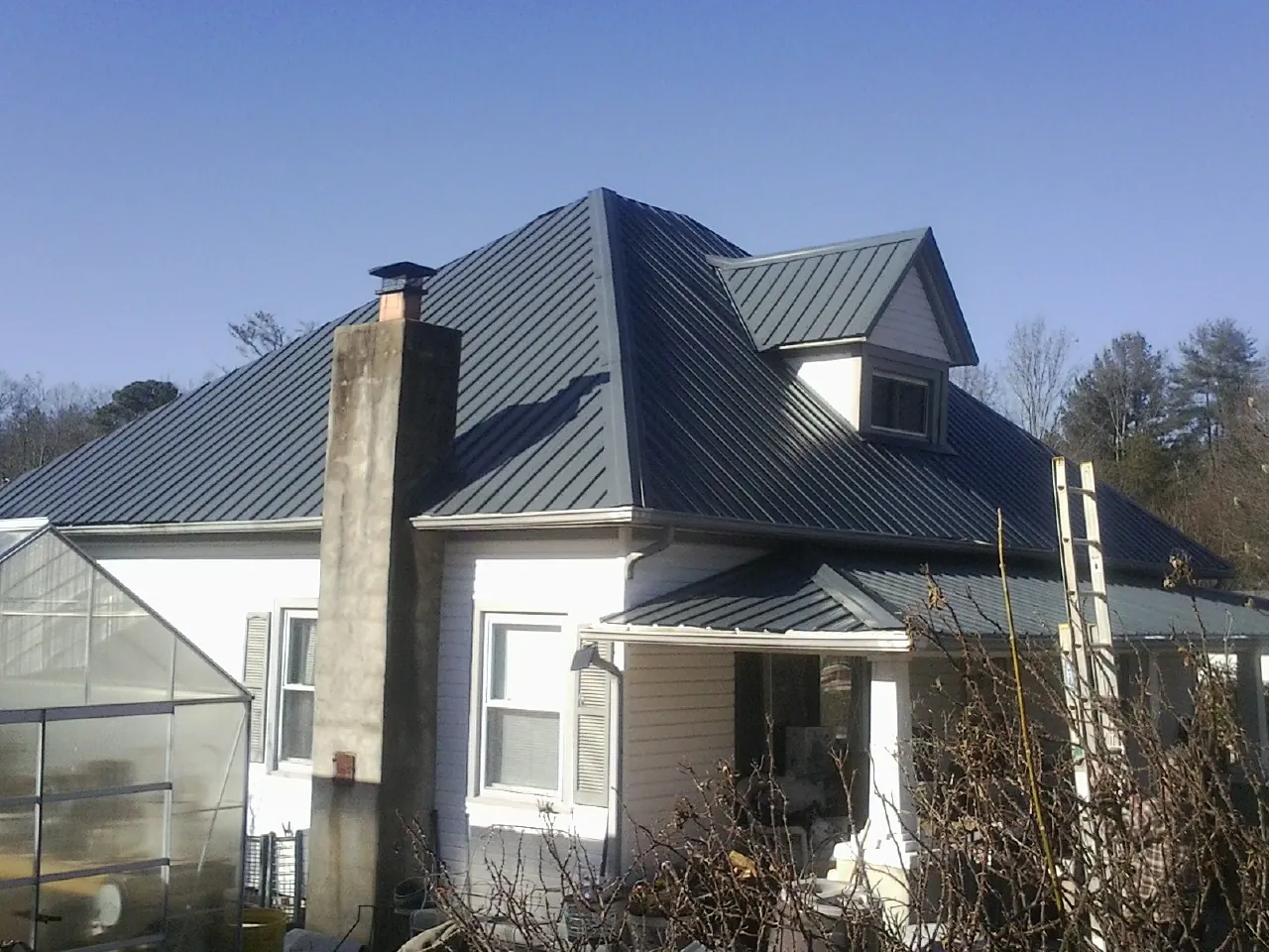 Dark blue standing seam metal roof on a white farmhouse with dormer — Slate & Tile Roof Repair by Roofing Brothers in Mc Causland