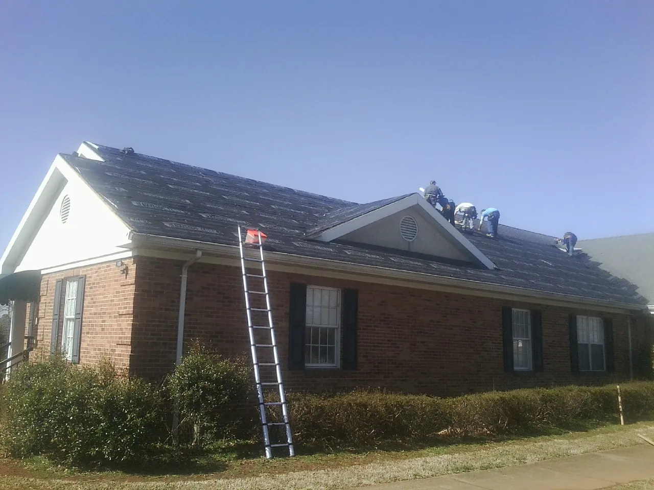 Crew tearing shingles off a brick ranch roof with a ladder set — Emergency Roof Repair work by our crew in Mc Causland