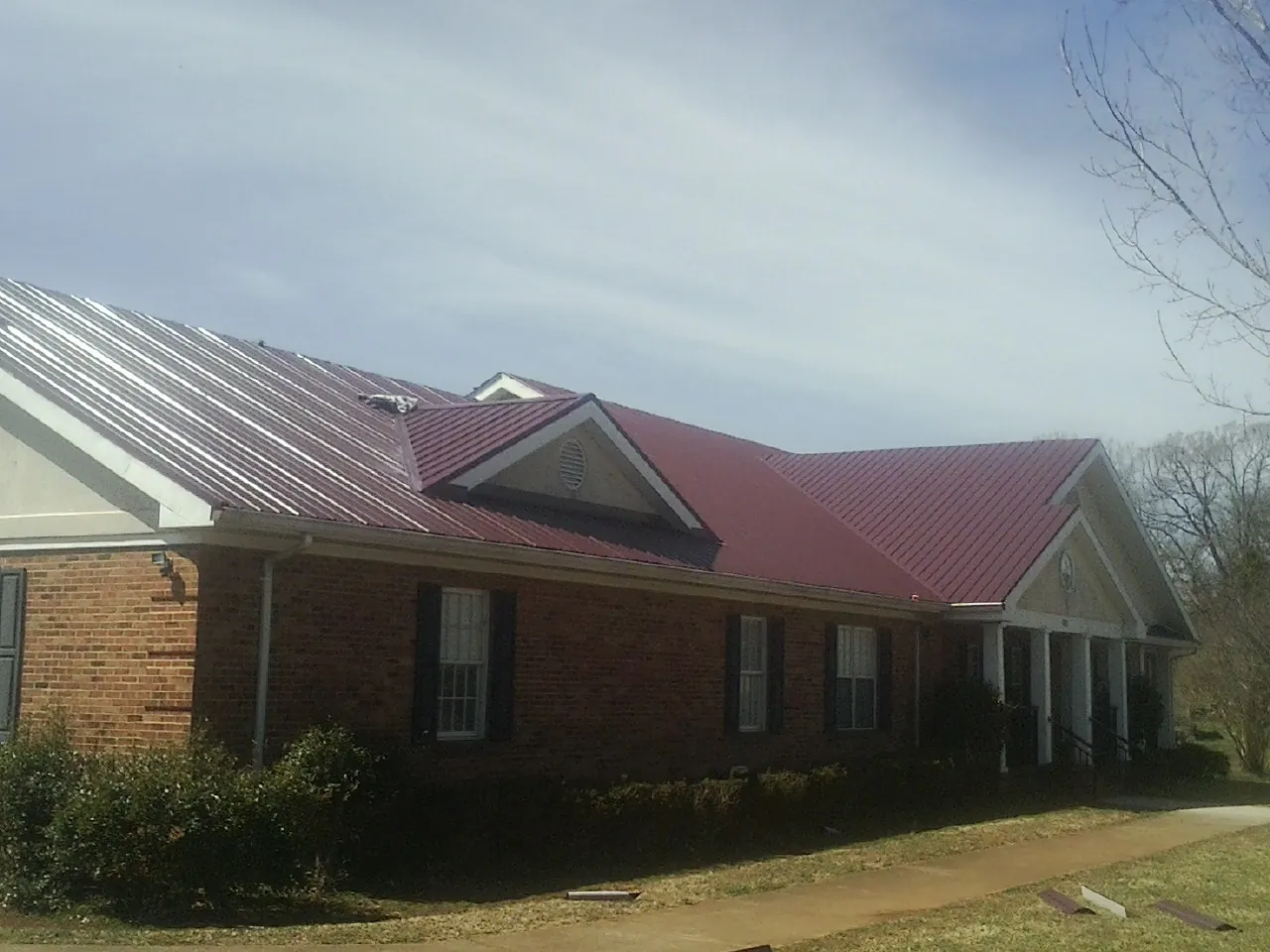 Red metal roof with gabled entries on a long brick building, from a Hail Damage Roof Repair job in Mc Causland