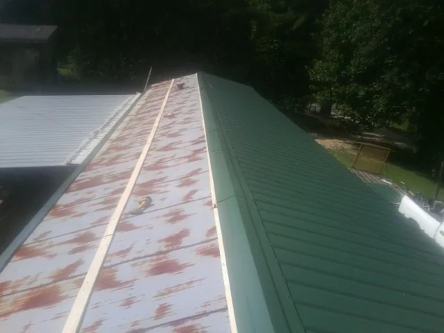 Old rusted panels beside newly installed green metal roofing — Wind Damage Roof Repair by Roofing Brothers in Mc Causland