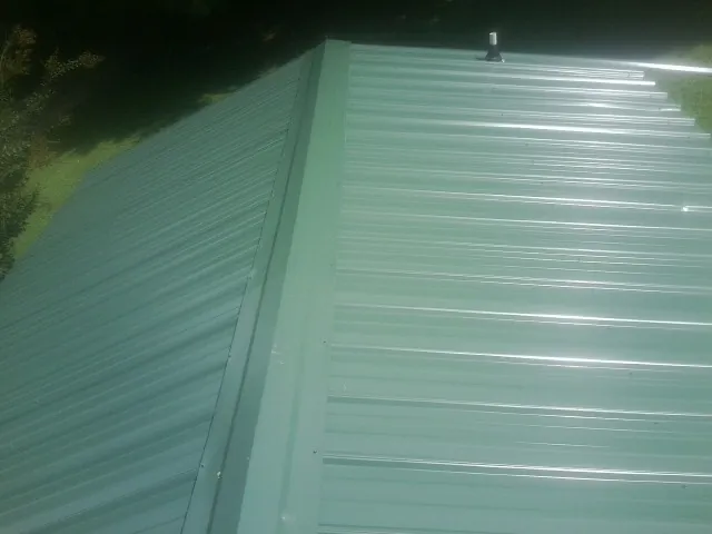 New green metal panels meeting at the ridge of a roof — Flat Roof Repair work by our crew in Mc Causland