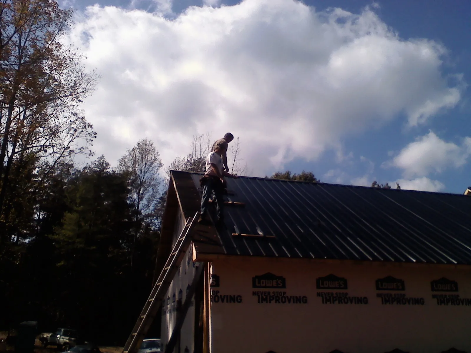Roofer fastening dark metal panels high against a cloudy sky, from a Roof Inspection job in Mc Causland