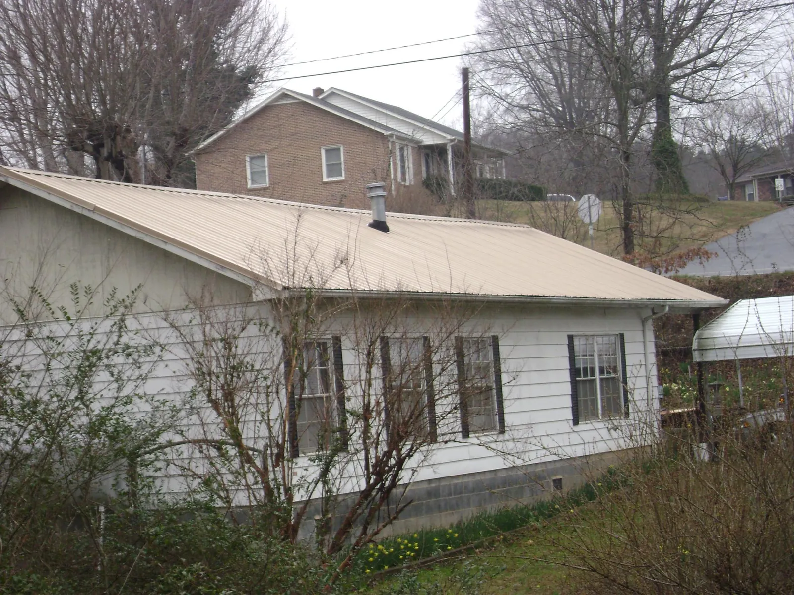 Tan metal roof on a white sided house set into a hillside — Commercial Roofing by Roofing Brothers in Mc Causland