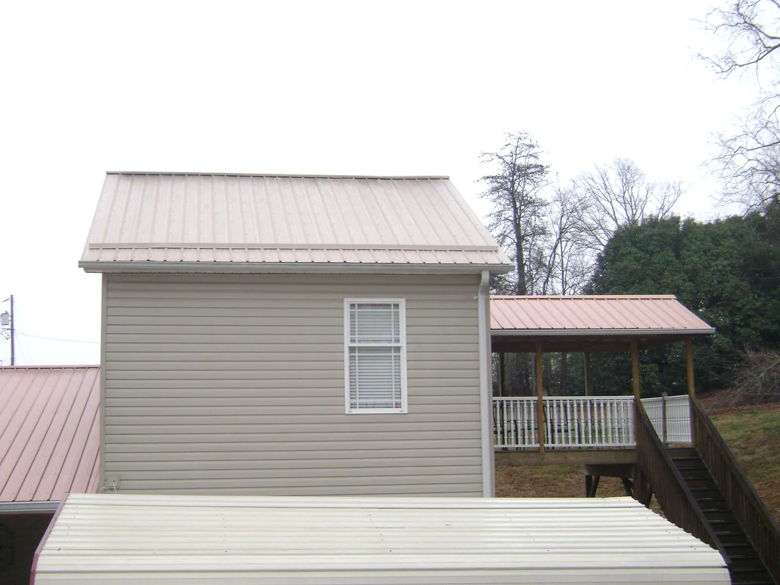 Tan metal roofs on a two story addition and attached porch, from a Roof Replacement job in Mc Causland